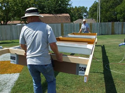 Image: Lifting spirit up — Italy ISD maintenance crewman Michael Chambers and Italy ISD School Board member Curtis Riddle (in the cowboy hat) rotate the frame used to mark of the squares to be painted in the endzone.