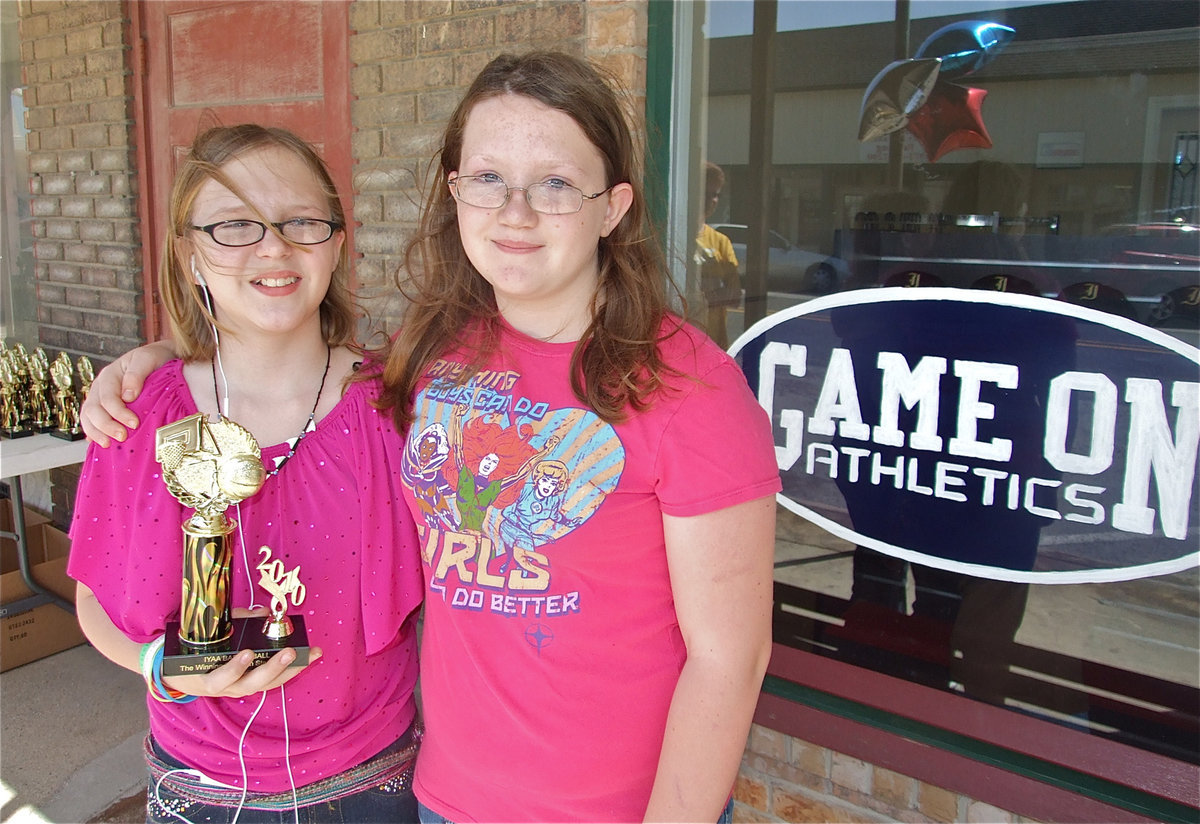 Image: Jen and Samantha — Accompanied by her friend Samantha Owen, Jennifer McDaniel receives her IYAA Basketball trophy and poses next to the Game On Athletics sign.