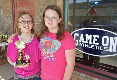 Image: Jen and Samantha — Accompanied by her friend Samantha Owen, Jennifer McDaniel receives her IYAA Basketball trophy and poses next to the Game On Athletics sign.