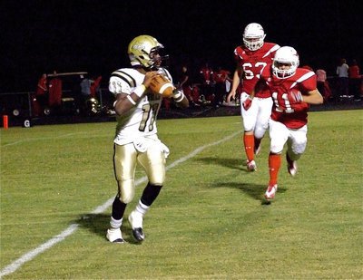 Image: Looking downfield — Jasenio Anderson(11) rolls right and searches for a receiver downfield while Axtell’s Ryan Linkous(11) and Jeremy Riser(63) put on pressure.