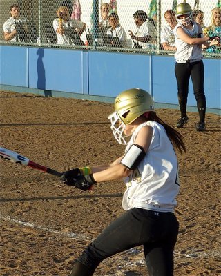 Image: 14’s a hitter — Drew Windham(14) drives one past the Lady Rattler infielders as her Lady Gladiator teammates urge her on from the dugout.