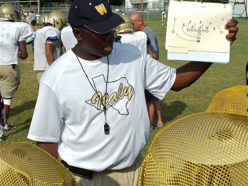 Image: Coach calls play — Coach Erik Wilson shows a running play to the JV huddle.
