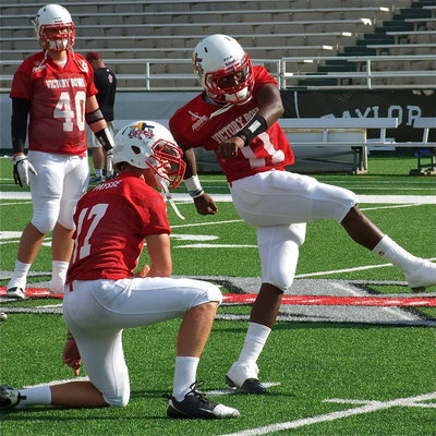 Image: Dawson’s, Nick Renfro(40), looks on as Belton’s, Jonathan Paysse(17), holds for Italy’s, Jasenio Anderson(11), as Anderson practices field goal kicks before the start of the Victory Bowl.