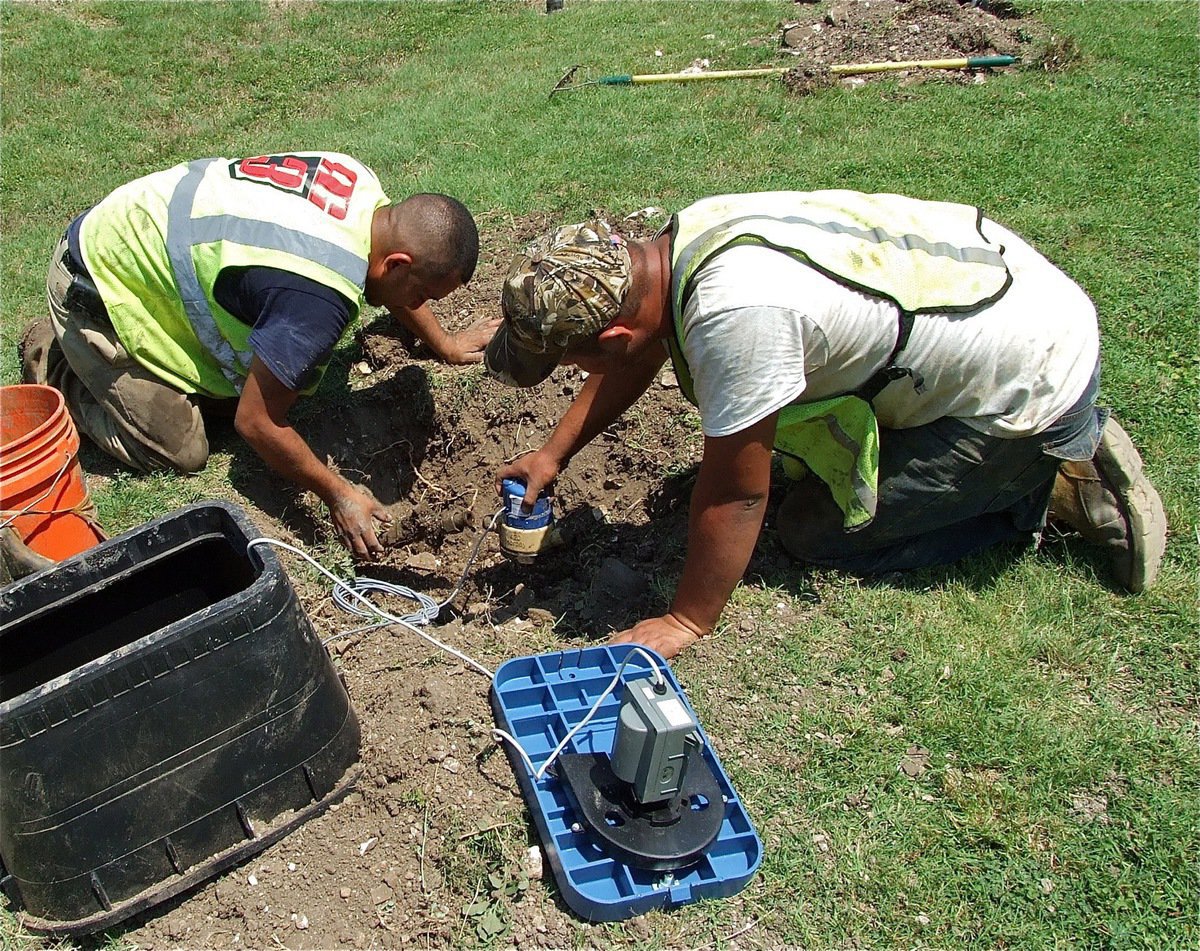 Image: Efrain Ramirez and Luis E. Caro Delgado work in tandem to install a new sensor driven Smart Meter along Harpold Street.