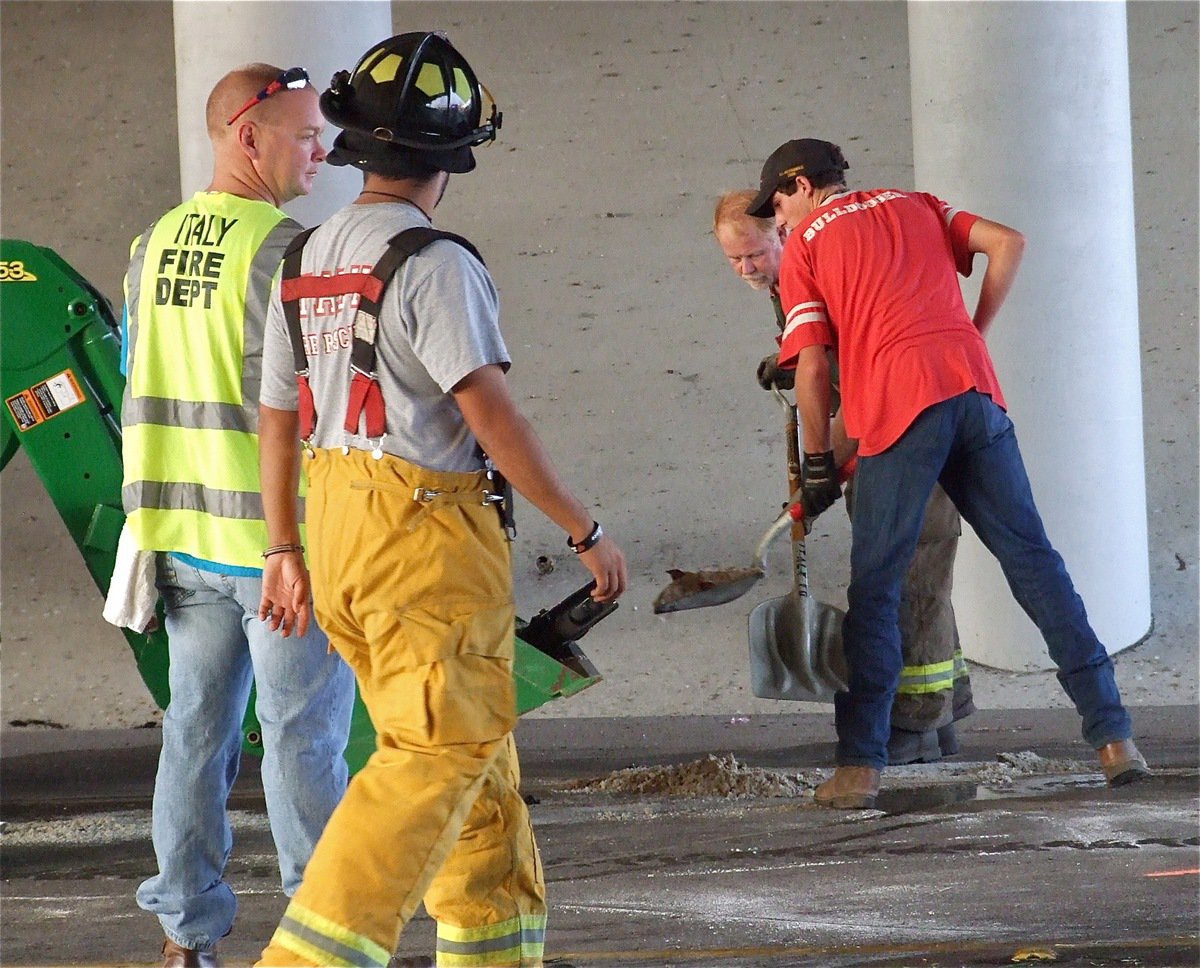 Image: Russell Helms of Helms Garage and IFD’s Red Buchanan shovel diesel fuel residue and debris from the roadway as Michael Chambers and Michael Martinez plan the crew’s next moves.