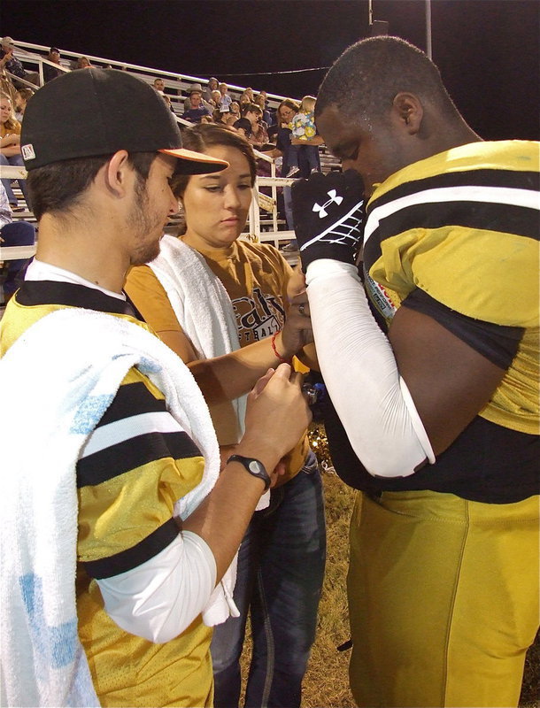 Image: Senior teamwork: Caden Jacinto(6) and Alyssa Richards help Adrian Reed adjust his shoulder pads during the game.