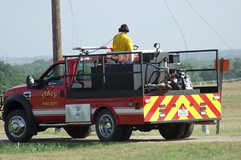 Image: After reaching the scene along Highway 77 and Martinez Road, Italy firefighters Brad Chambers, at the wheel, and Brandon Jacinto, manning the hose, communicate via headphones to avoid dangling power lines in an effort to saturate the resulting grass fire with water.