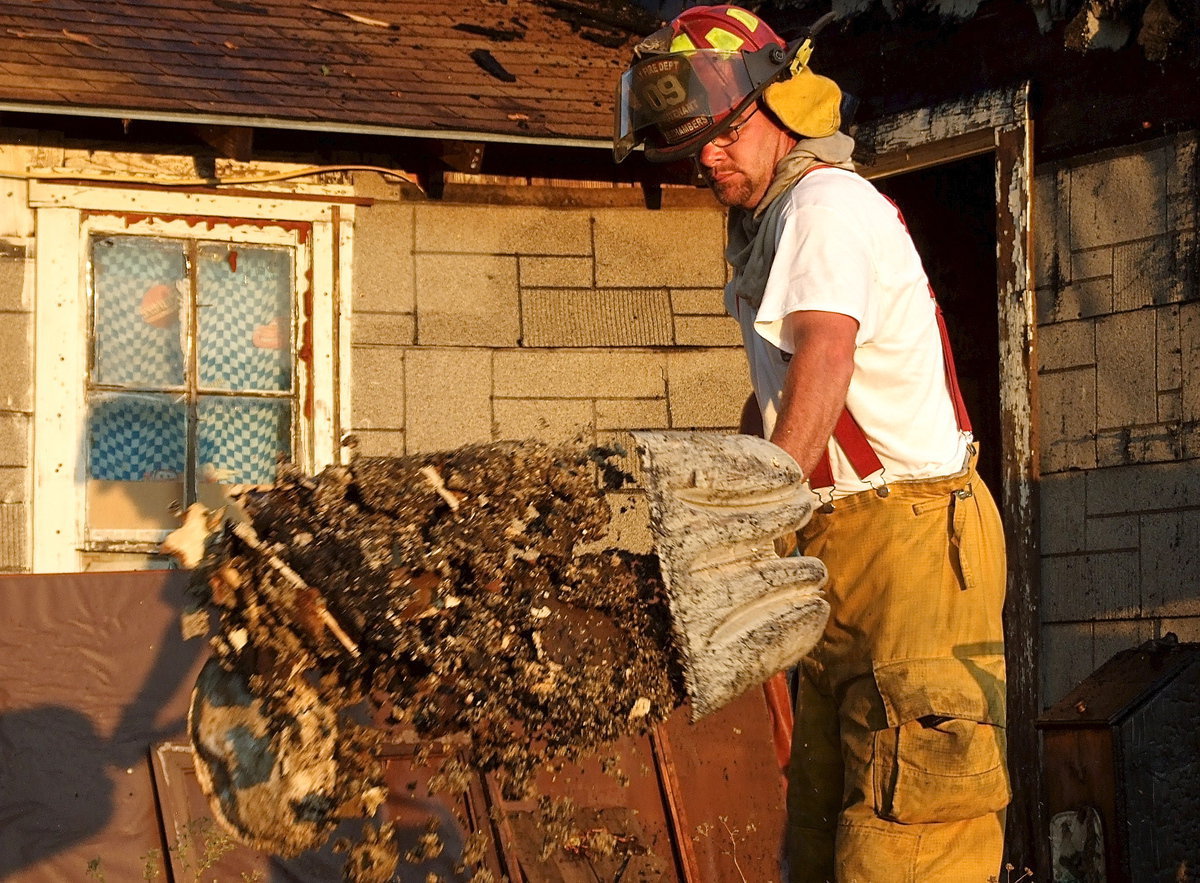 Image: Italy firefighter, Brad Chambers, shovels a load of debris on a pile being watered down.