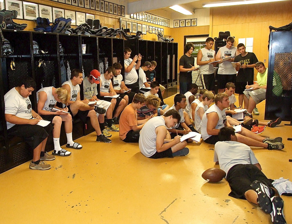 Image: Several football players copy down practice plays.