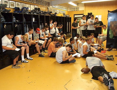 Image: Several football players copy down practice plays.