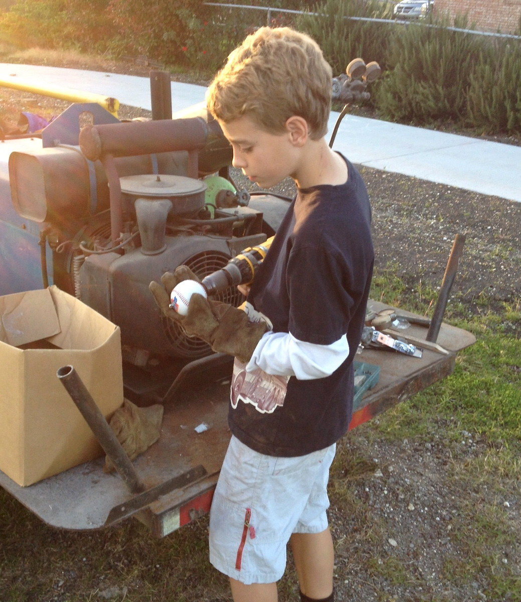 Image: Creighton Hyles drills holes thru the center of baseballs in order to pass a cable thru the core. The balls will help everyone to identify the cable wire which separates the walking trail from the parking area.