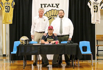 Image: AD/HFC, Charles Tindol, and Italy ISD Superintendent Jaime Velasco support Zain Byers as Zain signs his commitment letter to play football for the Austin College Kangaroos.