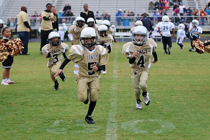 Image: Damien Wooldridge(5), Gared Wood(4), Kace McDaniel(3) lead their C-team Gladiator teammates off the field and thru spirit alley after their opening day shutout win over Rice.