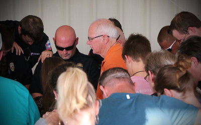 Image: First Baptist Church of Italy Pastor Ronnie Dabney brings together local police and fire personnel along with supportive citizens to form a tight group in a display of unity during the ceremony’s final prayer.